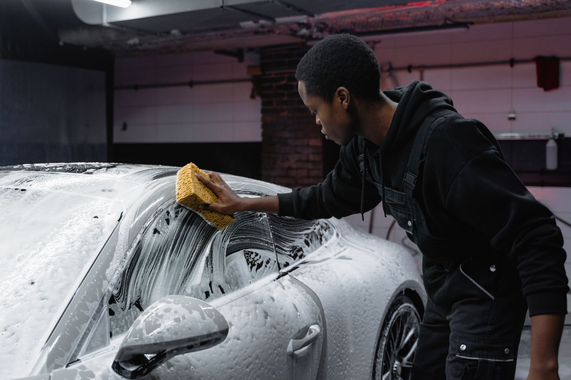 Car being hand-washed with thick shampoo suds under workshop lighting